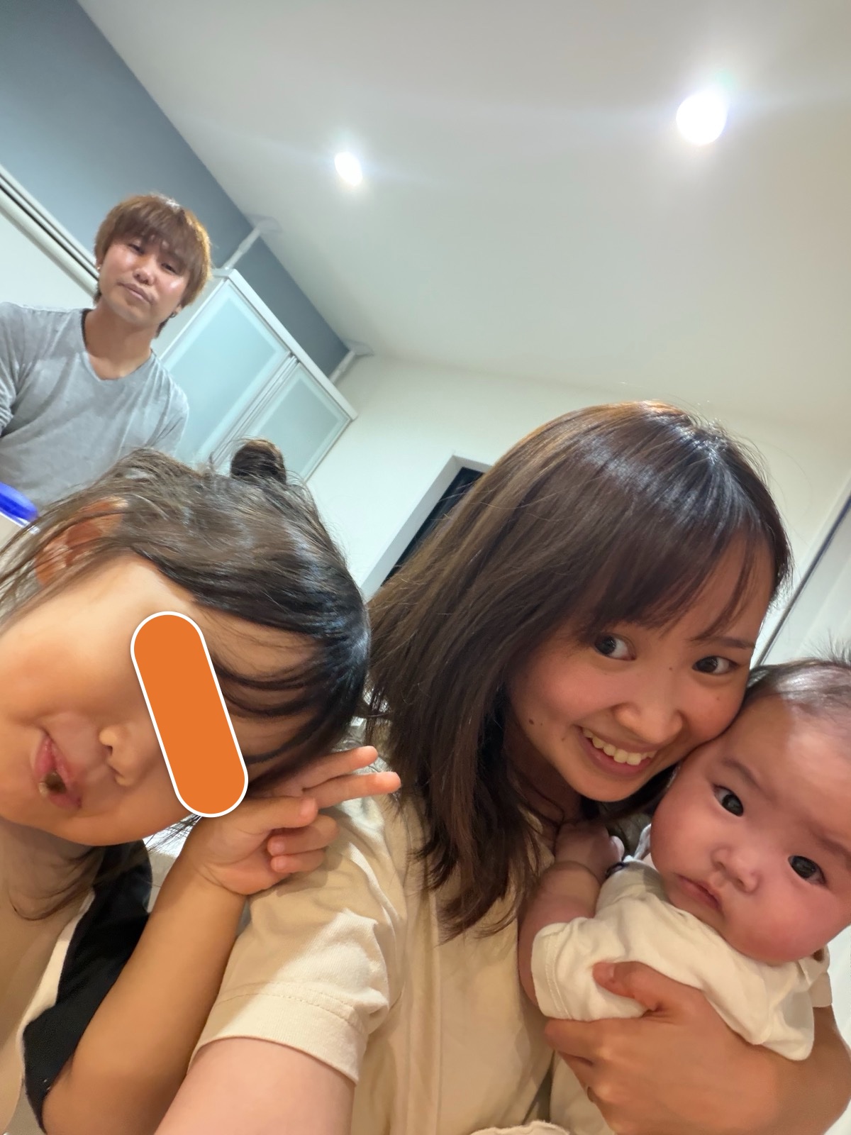リビングで自撮りした家族4人。手前に娘と赤ちゃんを抱いた母、奥に父